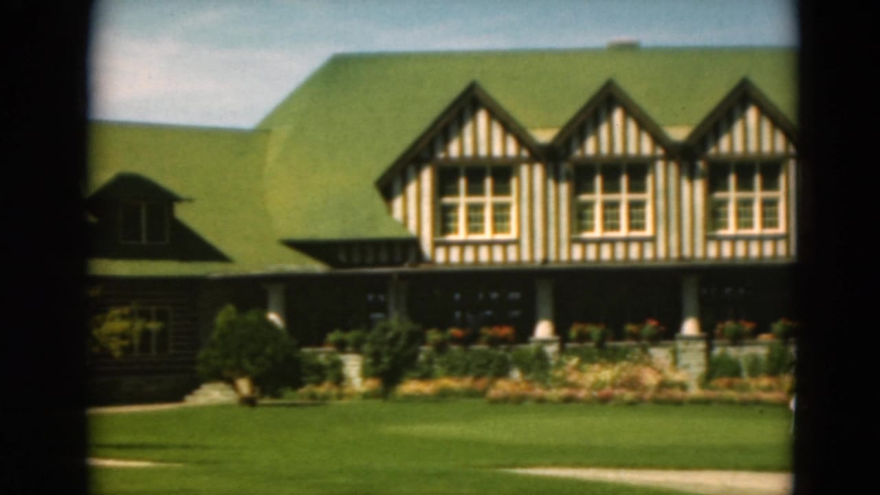 Striped timber gables and green roof above a porch, lawn, shrubs, and flowerbeds.