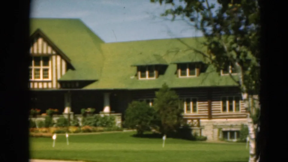1975 Duluth frame of the house exterior, showing Tudor trim, log-style siding, porch columns, lawn, and tree cover.