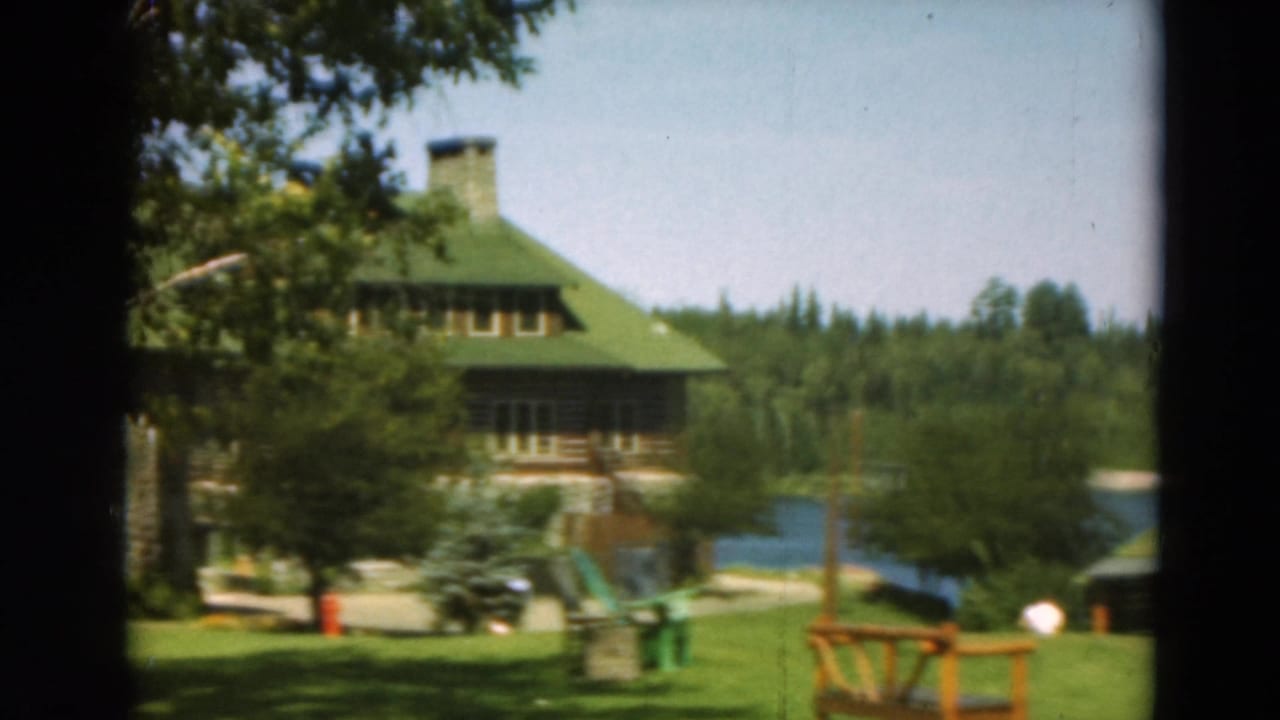 Green-roofed lodge and lawn with lake water visible at right.