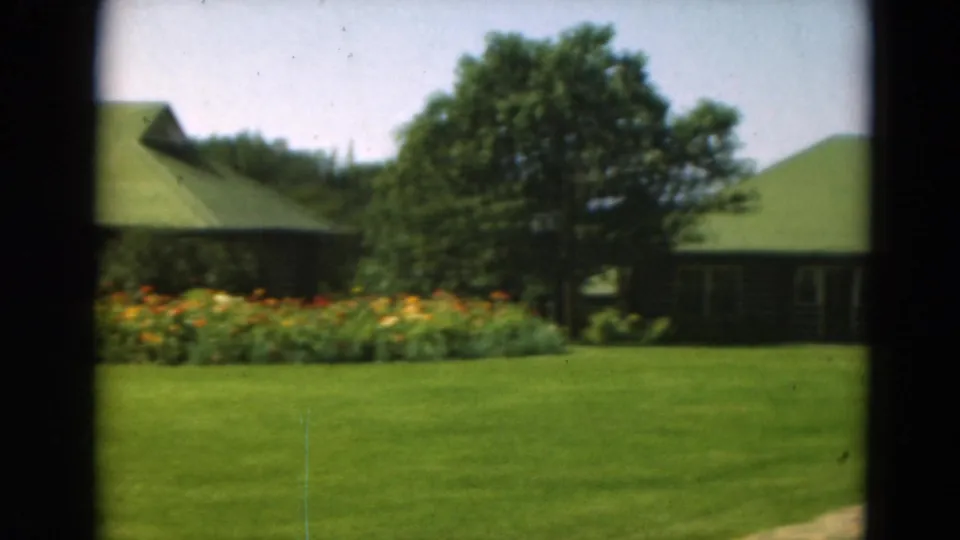 1975 8mm frame of resort lawns, a colorful flower bed, trees, and green-roofed lodge buildings in Minnesota.