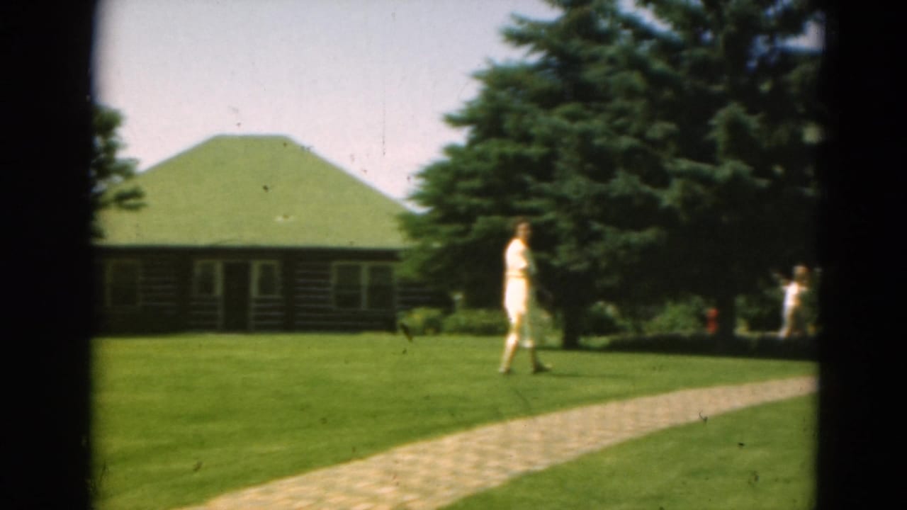 Woman in a light dress walks across resort-like grounds in Duluth, Minnesota, with a green-roofed cabin behind her.