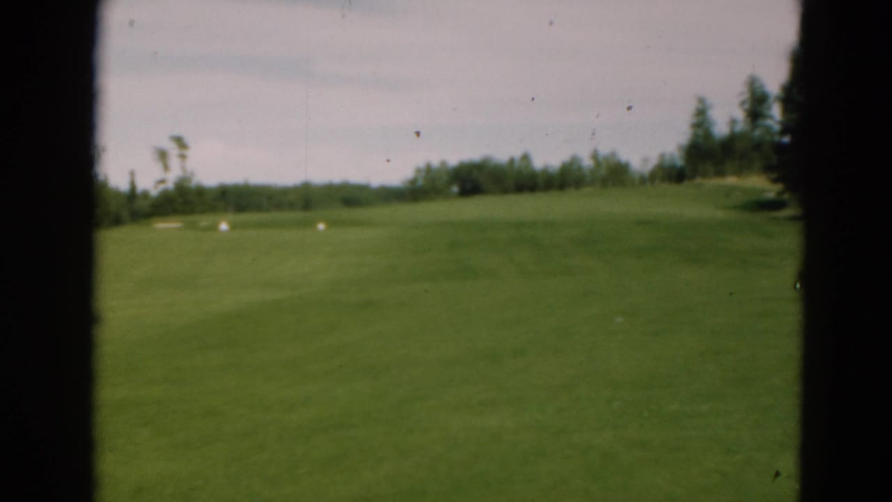 A 1975 Duluth golf-course view on 8mm film, showing an open fairway, distant trees, pale sky, and heavy dark frame borders.