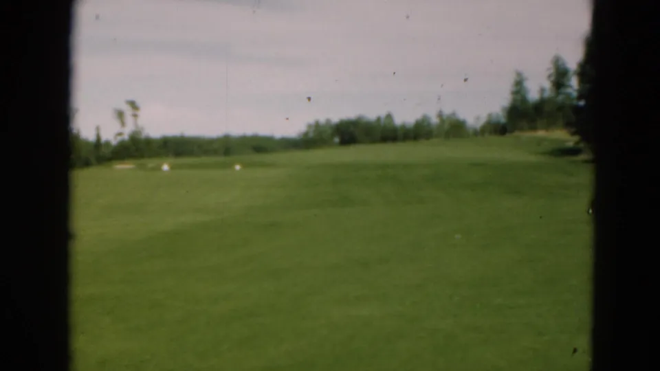 A 1975 Duluth golf-course view on 8mm film, showing an open fairway, distant trees, pale sky, and heavy dark frame borders.