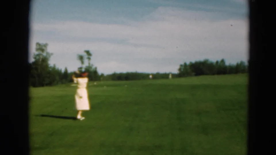 The woman in a light dress and red hat lifts her club during a golf swing on the Duluth course.