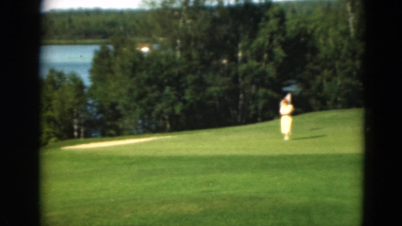 Golfer on a green fairway with a lake and trees behind dark frame edges.