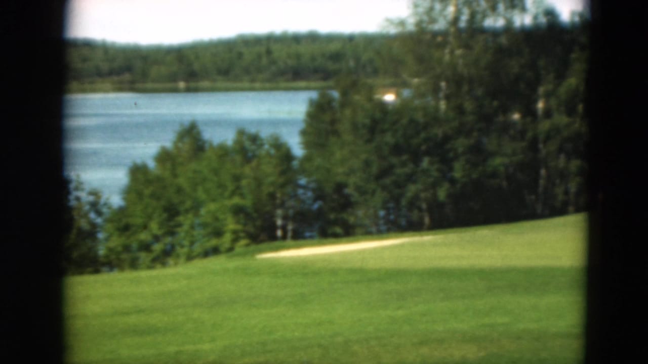 Green golf fairway with a sand trap, lake, trees, and dark frame edges.