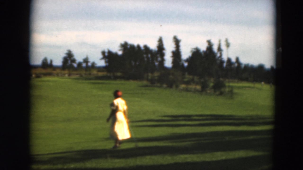 A woman in a yellow dress walks across a Duluth golf course in metadata-supported 1975 8mm footage.