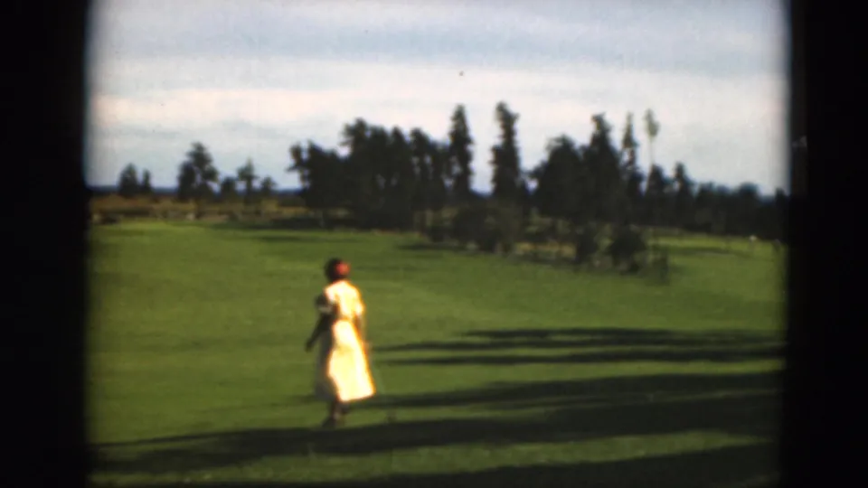 A woman in a yellow dress walks across a Duluth golf course in metadata-supported 1975 8mm footage.