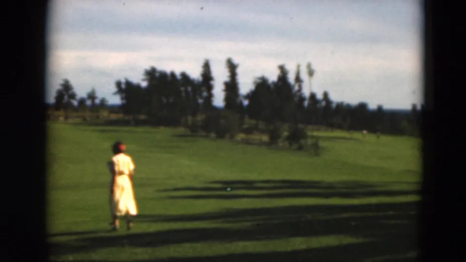 The woman appears near the left of the frame on a green Duluth fairway, with trees and long shadows behind her.