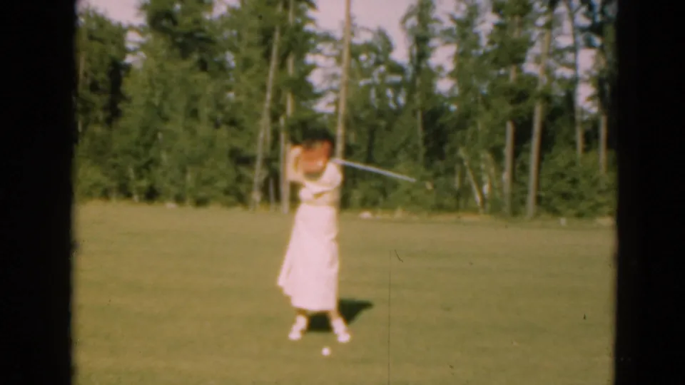 In 1975 Duluth, Minnesota, a woman in a light dress appears mid-swing on a sunlit golf course with pine trees behind her.
