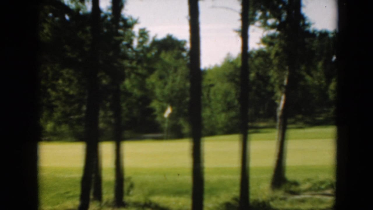 1975 8mm golf-course frame with a distant white flag visible across a green fairway in Duluth, Minnesota.