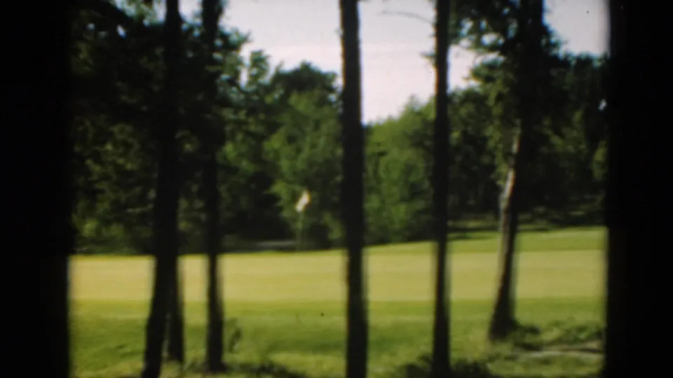 1975 8mm golf-course frame with a distant white flag visible across a green fairway in Duluth, Minnesota.