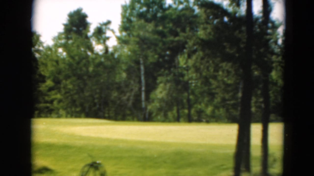 Green open lawn bordered by tall trees, seen through dark film-gate edges.