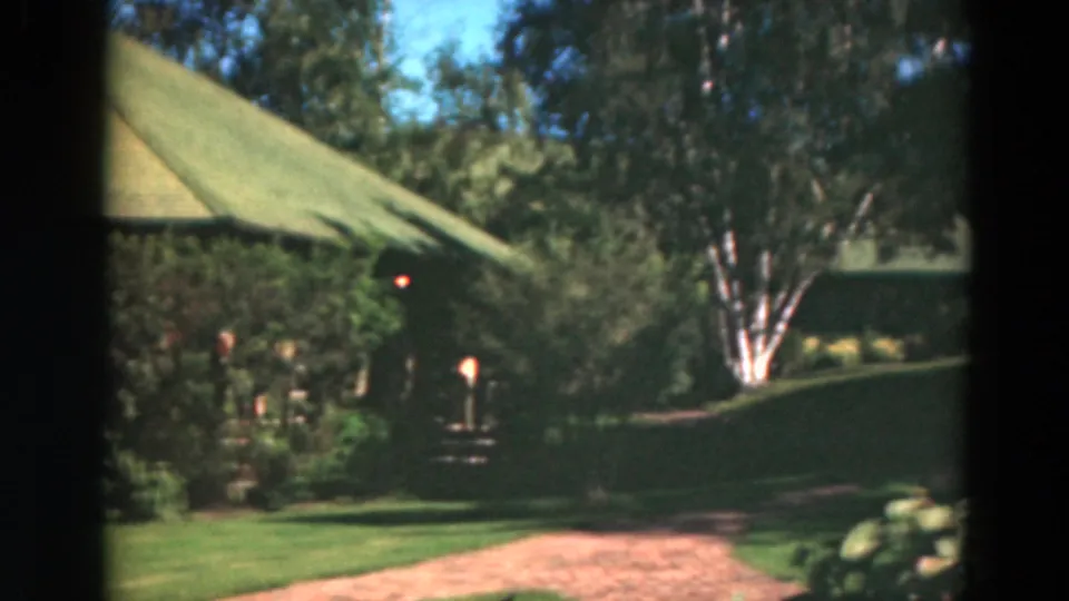 1975 Duluth frame ending on the landscaped grounds, with a birch tree, brick path, shrubs, and part of the green-roofed house.
