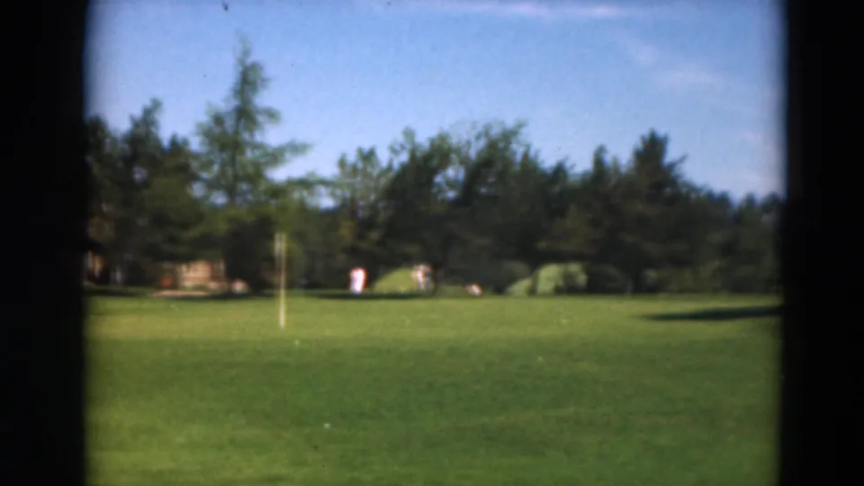 1975 Duluth golf-course frame showing a fairway, flagstick, trees, and distant golfers in light-colored clothing.