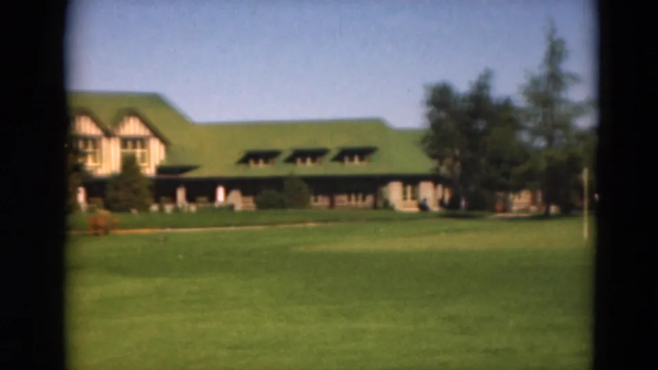 Closer 1975 Duluth golf-course view showing the green-roofed lodge-like building, fairway, trees, and soft 8mm color.
