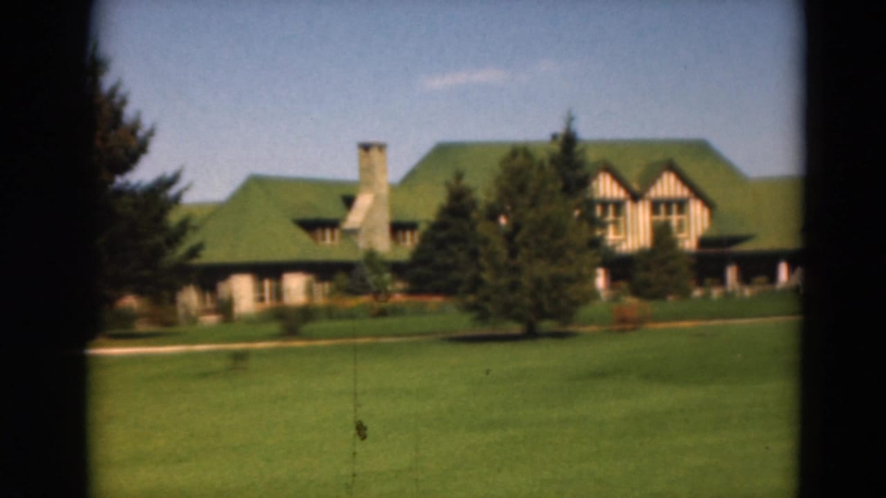 Green-roofed building and evergreens viewed across a manicured lawn.