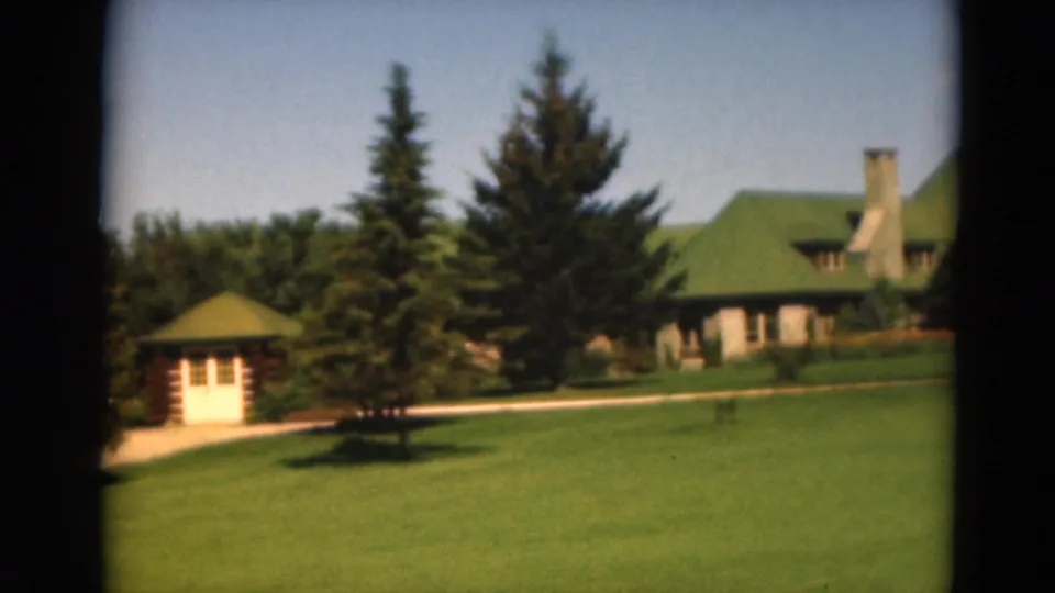 The final 1975 Duluth frame shows a small pavilion-like structure, tall evergreens, lawn, path, and part of the green-roofed building.