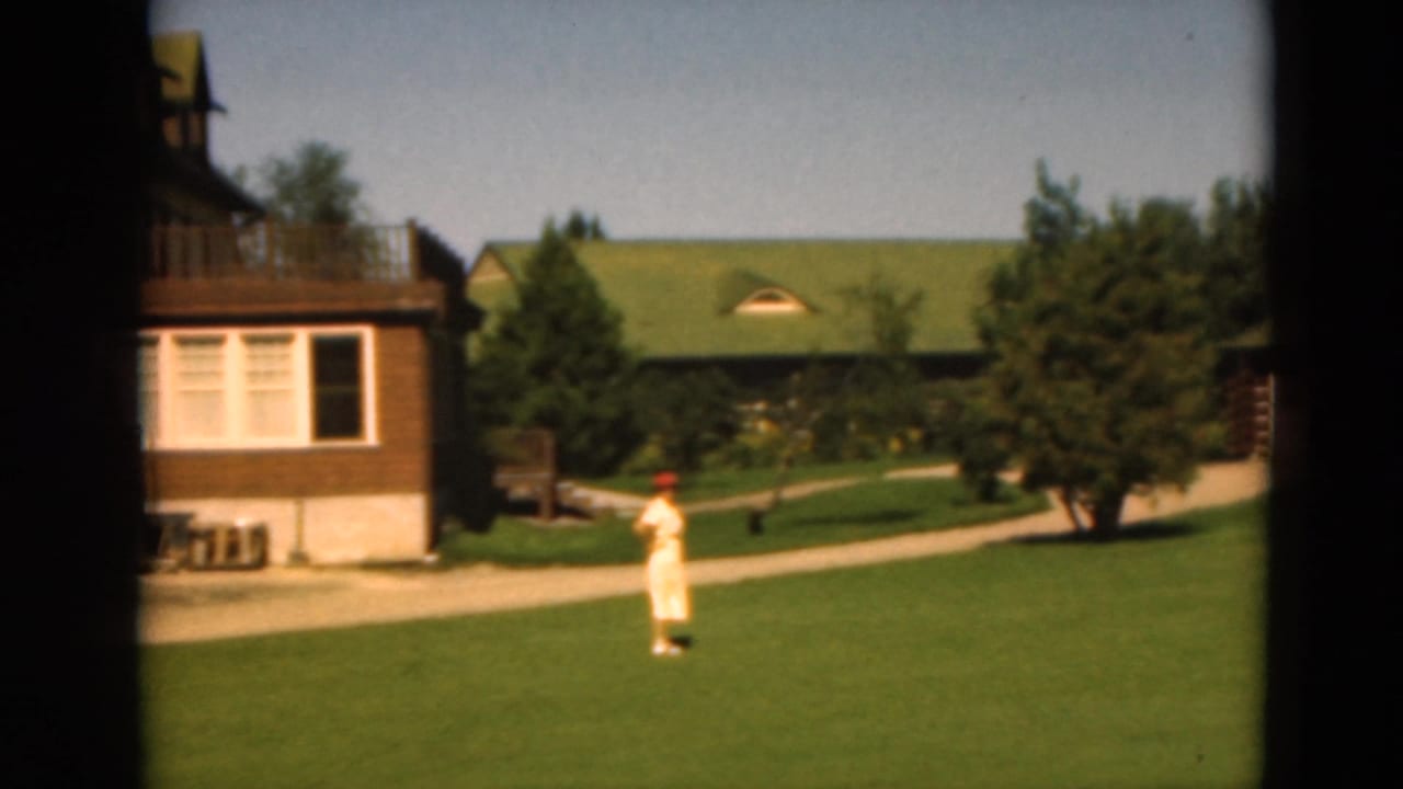 1975 Duluth 8mm frame showing green-roofed buildings, lawn, trees, and a distant woman in light clothing.