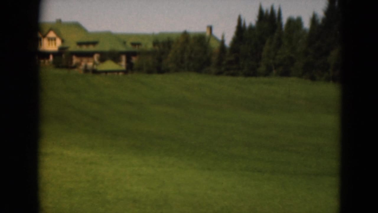 Wide lawn rising toward a green-roofed lodge-style building among trees.