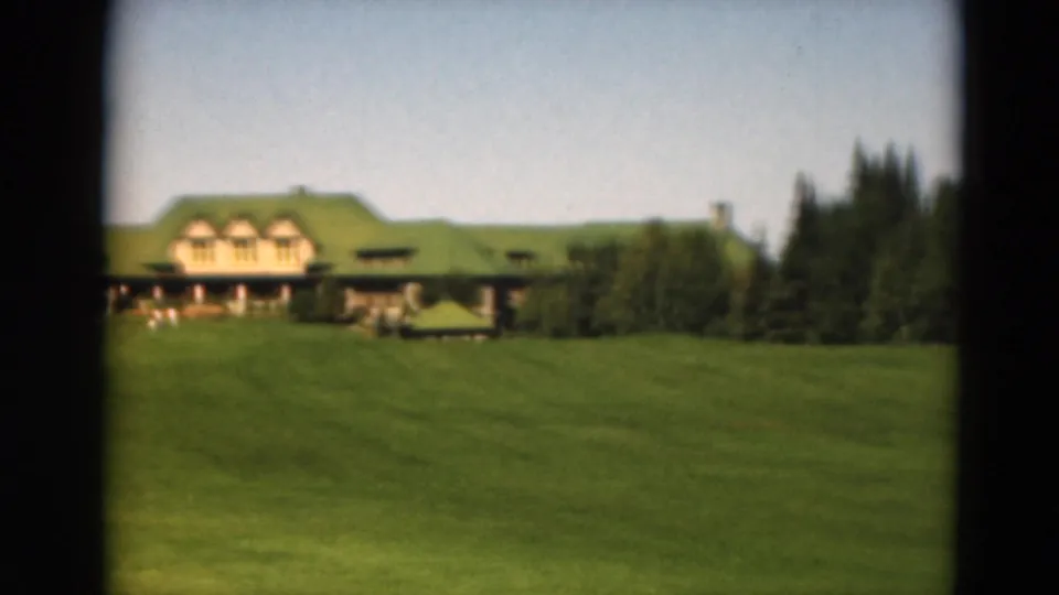 1975 Duluth 8mm view of a large green-roofed building across a grassy slope with trees at the side.