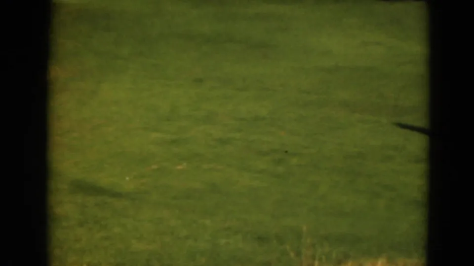 A soft 8mm frame from the Duluth golf course shows mostly green fairway, with the subject drifting below the clubhouse view.