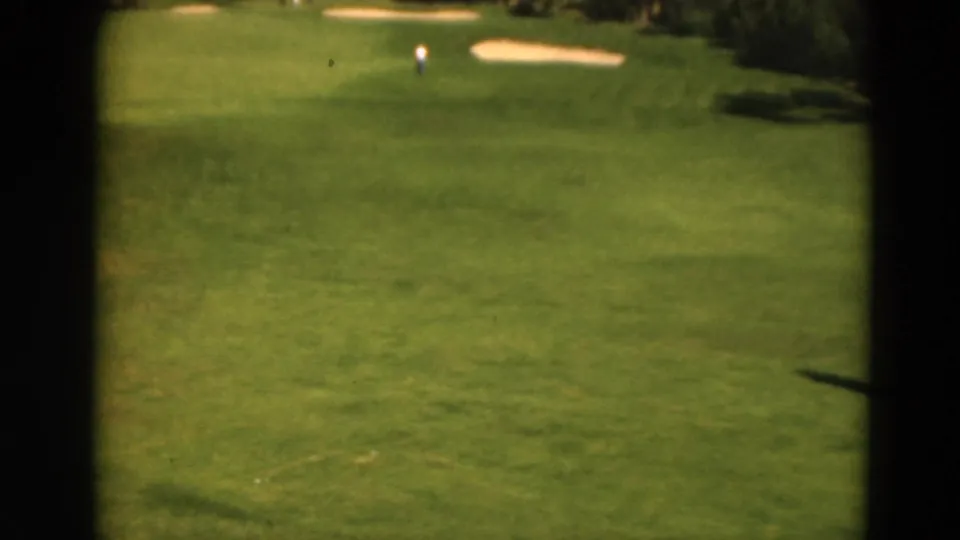 1975 Duluth golf course frame with fairway, sand traps, trees, and a distant person near the green.