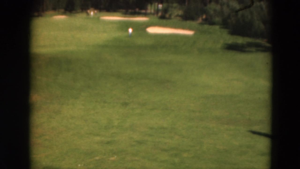 Wide fairway with sand bunkers, trees, and a distant golfer under bright sun.