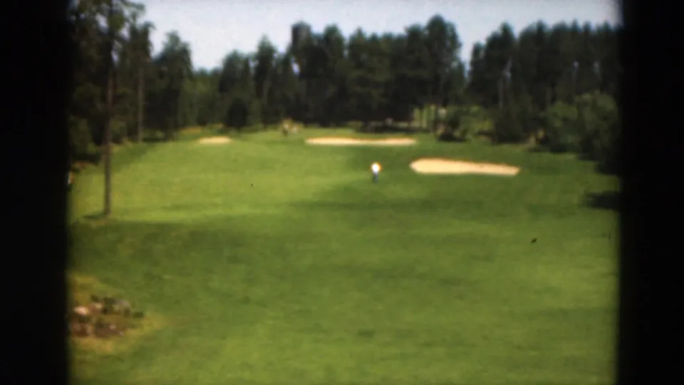 1975 Duluth 8mm frame of a golf course from a slightly lower angle, showing fairway, bunkers, trees, and a distant golfer.