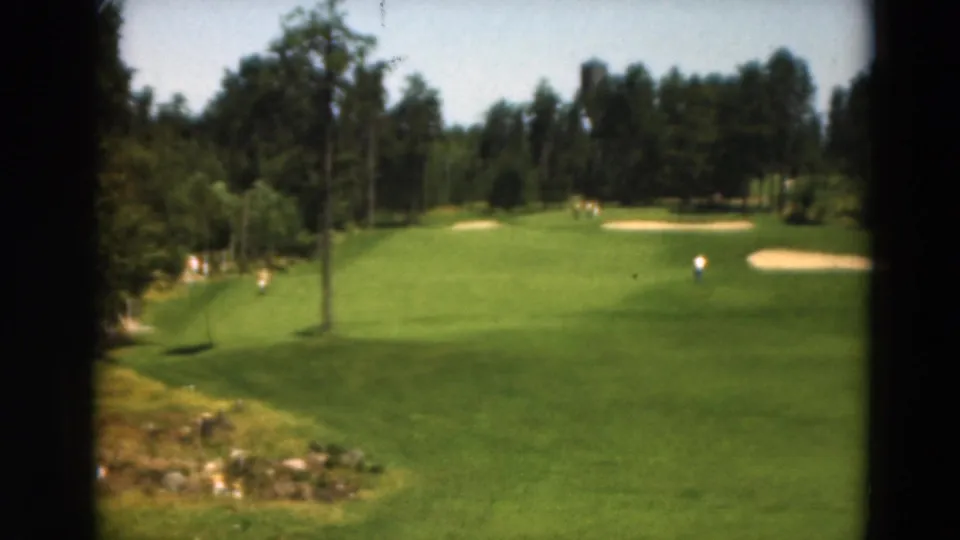 1975 Duluth 8mm view of a golf course with a sloping fairway, foreground rocks, bunkers, trees, and a distant golfer.