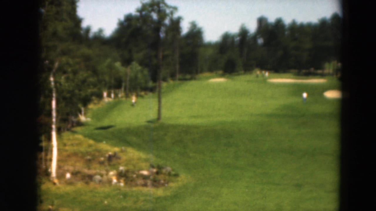 Wooded golf fairway with sand traps and a distant figure, framed by dark film edges.