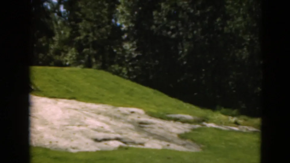 1975 Duluth 8mm frame showing the pan ending on a pale sand trap, curved green, and wooded edge of the course.
