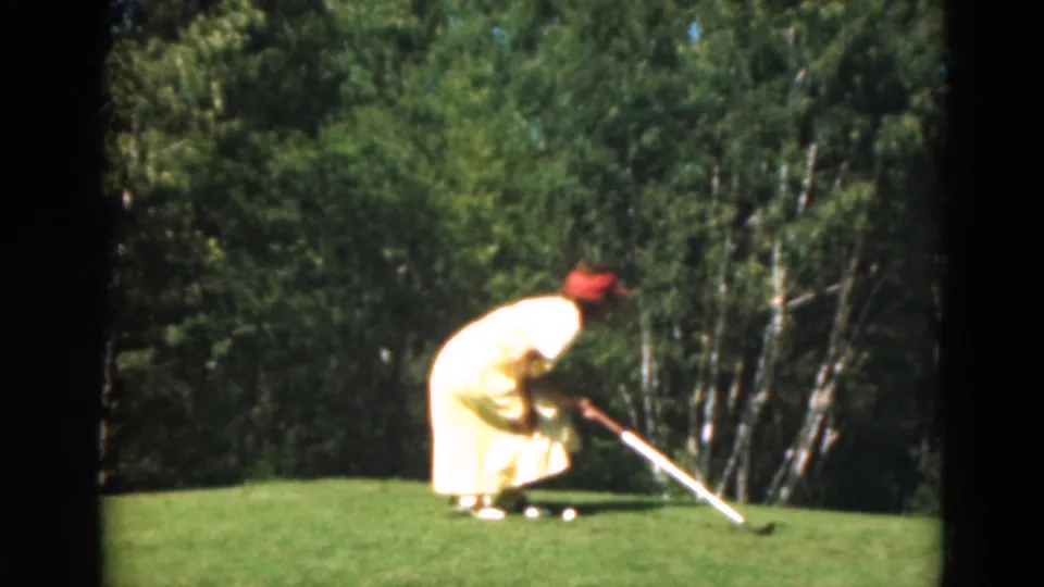 A 1975 Duluth home-movie frame shows the golfer bent over a putter on the green with trees behind the course.