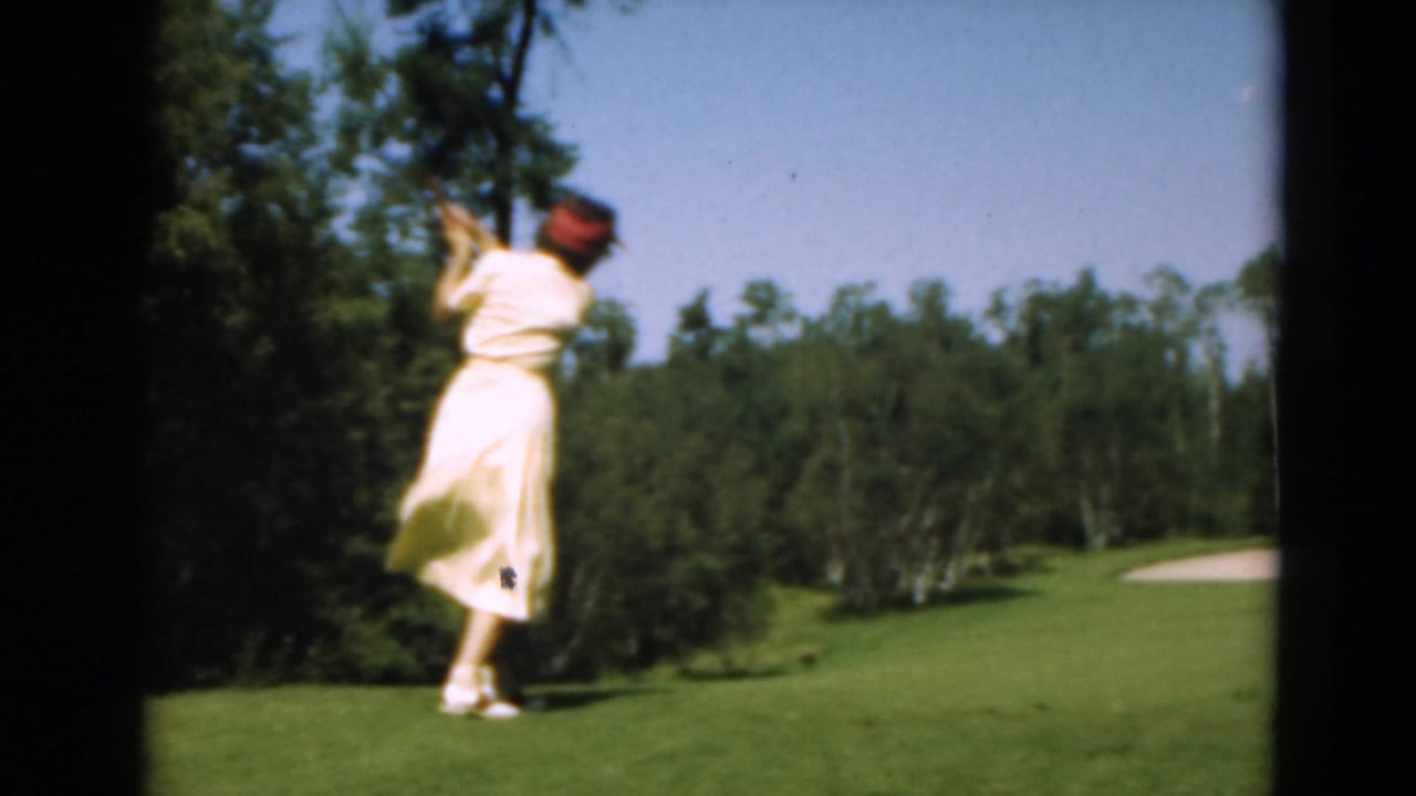 Woman golfer follows through with her club on a green course bordered by trees.