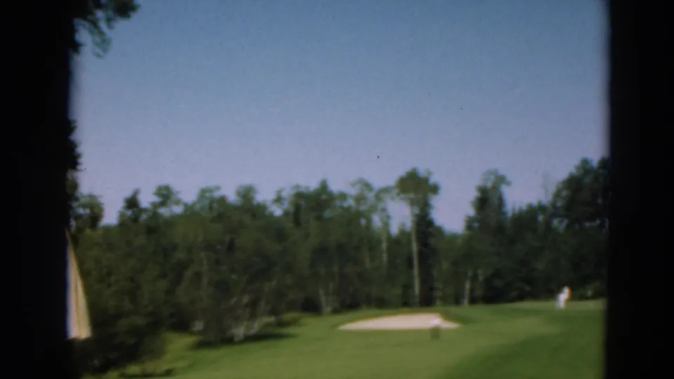A wider view of the Duluth golf course shows green fairway, a sand trap, tree line, and distant golfers or spectators.