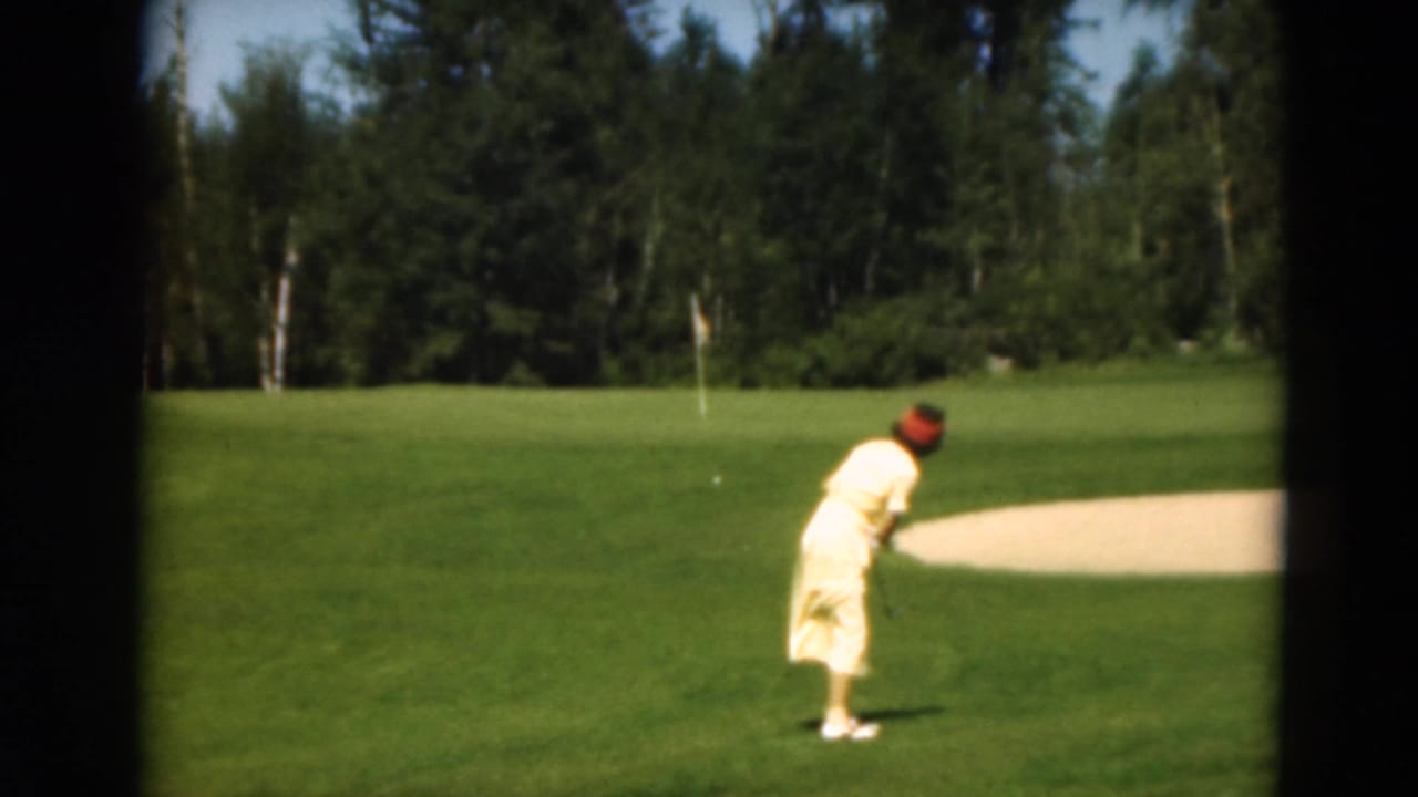 In Duluth, Minnesota in 1975, a woman in yellow stands on a golf course near a sand trap and tree-lined fairway.