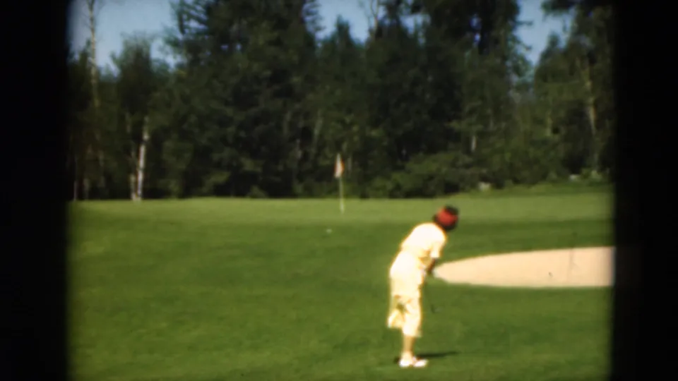 A woman in yellow appears ready to play a golf shot near a sand trap on a wooded Duluth course in 1975.
