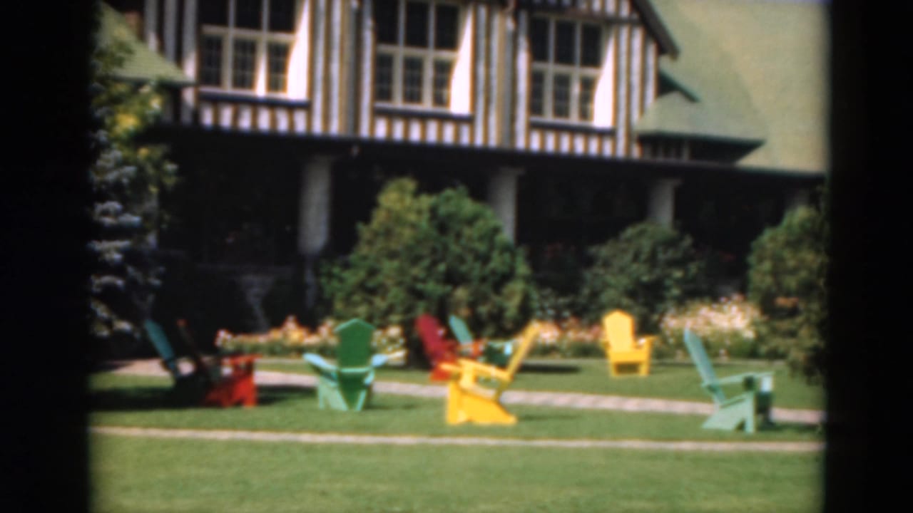 Resort building, lawn, shrubs, and colorful chairs near a garden path.