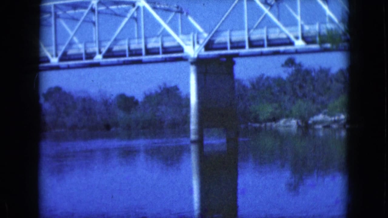 White truss bridge spans a calm river with trees along the opposite bank.
