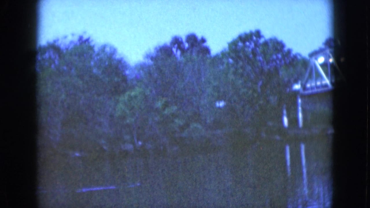 1975 Florida home-movie frame of a wooded river scene with a metal truss bridge cropped at the right edge.