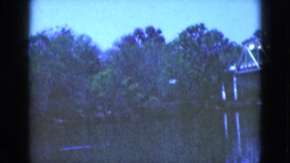 1975 Florida home-movie frame of a wooded river scene with a metal truss bridge cropped at the right edge.