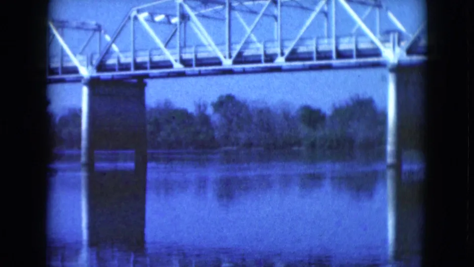 1975 Florida 8mm frame showing a white truss bridge over calm river water, with piers and reflections visible.