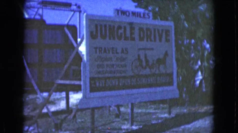 Blue-shifted 8mm frame of the Jungle Drive roadside attraction sign, partly soft but readable as a horse-ride advertisement.