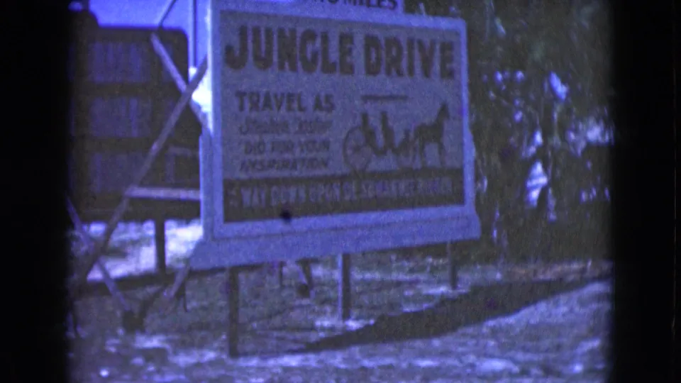 1975 Florida 8mm frame showing the Jungle Drive attraction billboard, Suwannee River wording, carriage artwork, trees, and handheld film framing.