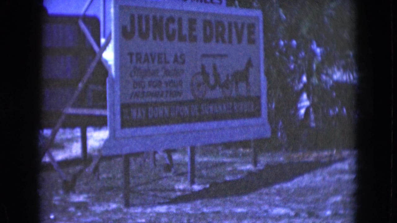 1975 Florida 8mm frame showing a Jungle Drive sign with a carriage illustration near trees and a dirt path.