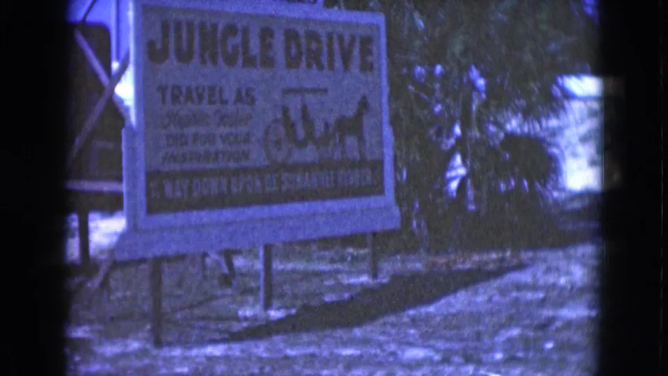 Blue-tinted 8mm view of the Jungle Drive sign, with carriage artwork and outdoor vegetation visible.