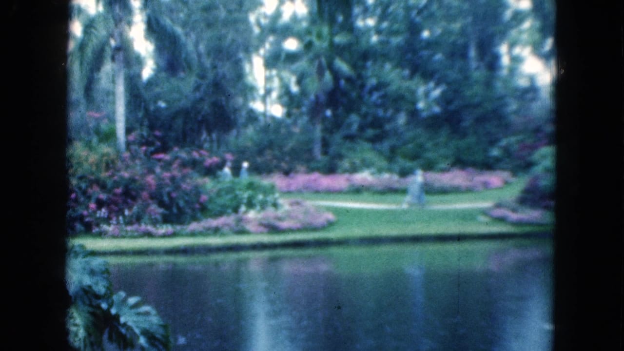Garden lake seen through dark vertical framing with flower beds and distant walkers.