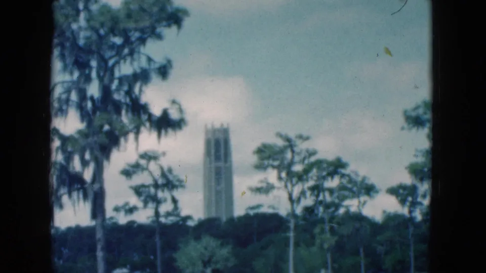 1975 Florida home-movie frame with a distant bell-tower-like structure seen through trees and soft blue-green color.