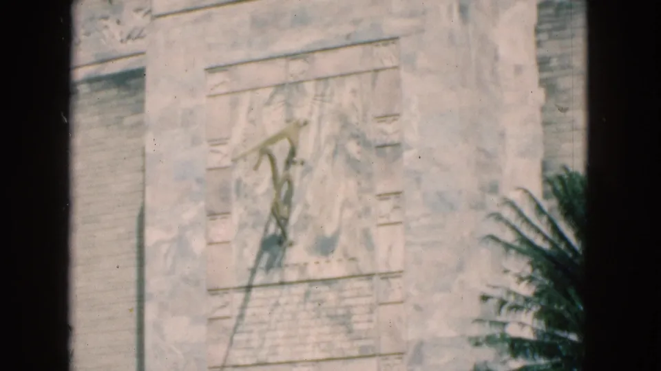 Close 8mm view of the Florida monument wall, showing weathered carving or inscription details and a palm frond in the foreground.