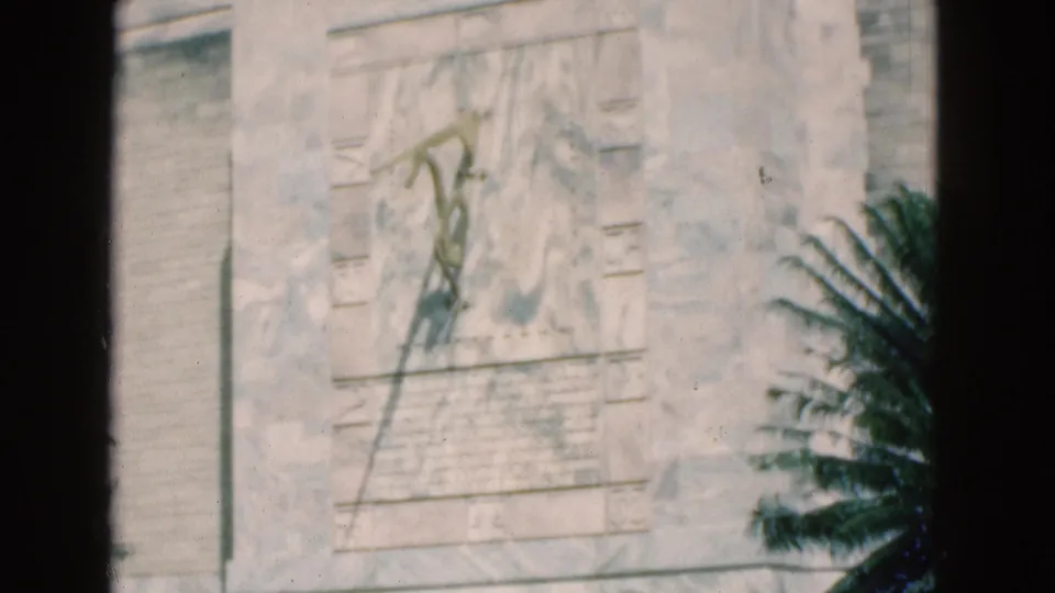 Final 1975 Florida frame holding on the carved monument wall, with pale stonework, partial inscription detail, and plants at the edge.